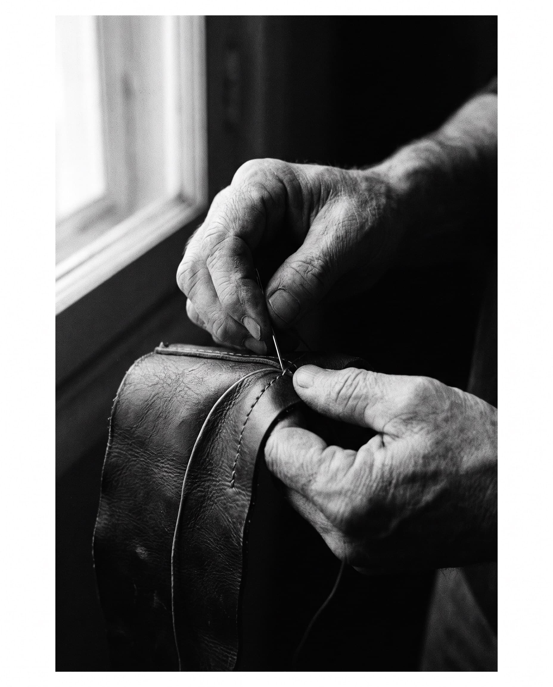 Weathered hands stitching by hand in low warm light.