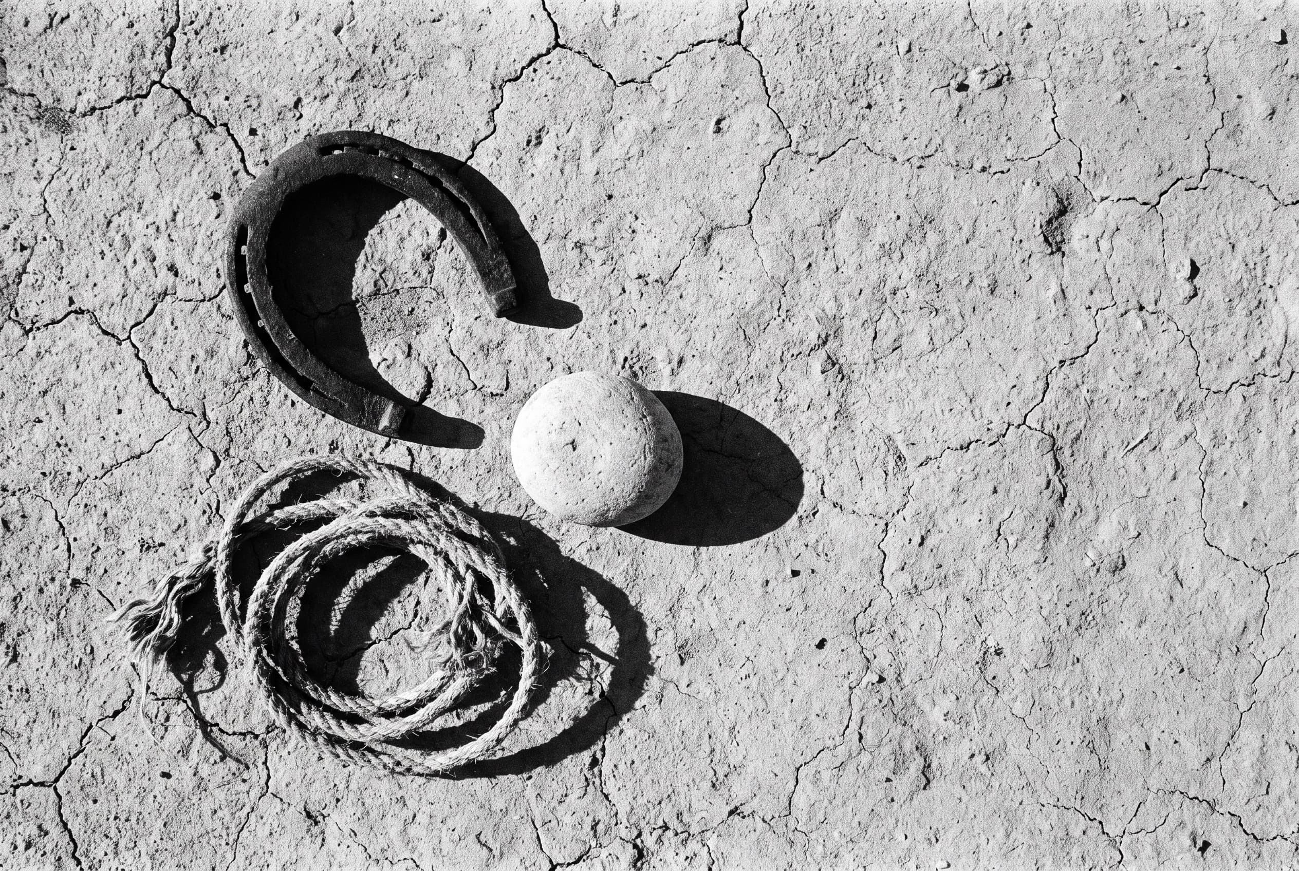 An iron horseshoe, coiled rope, and a stone arranged on cracked earth.