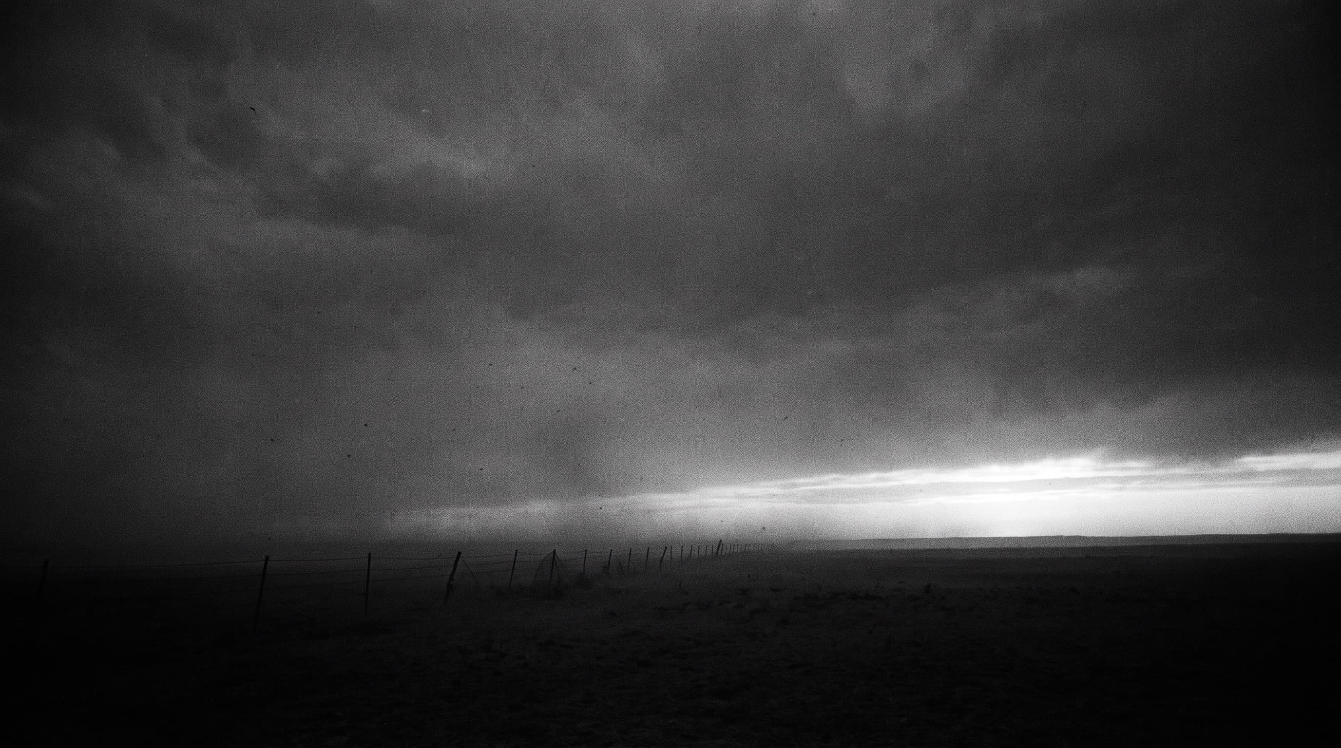 An empty Texas plain at dusk under a heavy sky, a distant fence line.